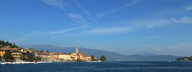Ferienwohnung beliebte Urlaubsziele am Gardasee -  Mit einer Fläche von 370 km² ist der Gardasee der größte See Italiens. Es liegt am Fuße der Alpen und erstreckt sich über drei Staaten: Lombardei, Venetien und Trentino. Die maximale Tiefe des Sees beträgt 346 m, er hat eine längliche Form und sein nördliches Ende ist sehr schmal. Dort ist der See von den Bergen der Gruppo di Baldo umgeben. Du trittst aus deinem gemütlichen Hotelzimmer und es begrüßt dich die warme italienische Sonne. Du blickst auf den atemberaubenden Gardasee, der in zahlreichen Blautönen schimmert - von tiefem Dunkelblau bis zu funkelndem Türkis. Majestätische Berge umgeben dich, während die Brise sanft deine Haut streichelt und der Duft von blühenden Zitronenbäumen deine Nase kitzelt. Du schlenderst die malerischen, engen Gassen entlang, vorbei an farbenfrohen, blumengeschmückten Häusern. Vereinzelt unterbricht das fröhliche Lachen der Einheimischen die friedvolle Stille. Du fühlst dich wie in einem Traum, der nicht enden will. Jeder Schritt führt dich zu neuen Entdeckungen und Abenteuern. Du probierst die köstliche italienische Küche mit ihren frischen Zutaten und verführerischen Aromen. Die Sonne geht langsam unter und taucht den Himmel in ein leuchtendes Orange-rot - ein spektakulärer Anblick.
